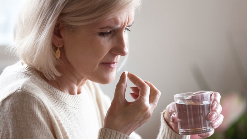Upset senior ill woman holding pill and glass or water taking painkiller medicine to relieve headache pain, sad middle aged elderly lady worried about side effects of meds for old person concept
