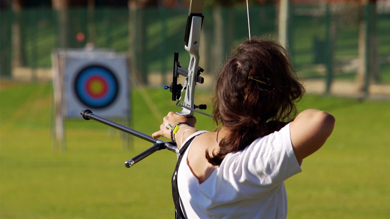 Back of archery athlete aiming at a target in the distance