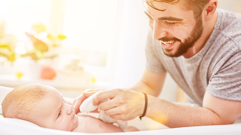 Father bathes baby in baby bath during his parental leave