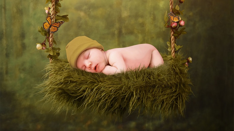 A young newborn baby is sleeping on a flower swing in an enchanted forest for a dream fairy concept.
