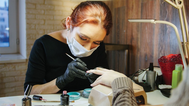 Labour of manicurist - nail master in medical mask doing professional manicure