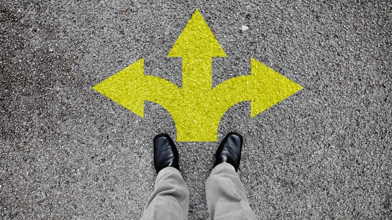 A pair of feet standing on a tarmac road with yellow arrow print pointing in three different directions for the concept of making decision at the crossroad.