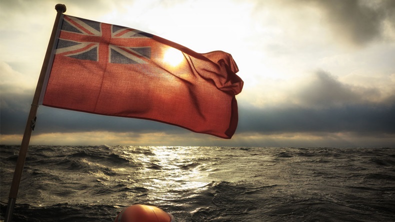 The UK red ensign the british maritime flag flown from yacht sail boat, stormy dark clouds sky and baltic sea. Summer and travel voyage