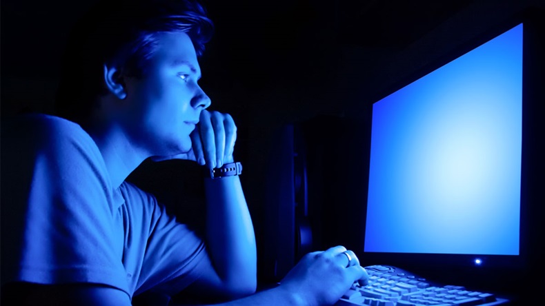 Man in front of computer screen. Dark night room and blue light.