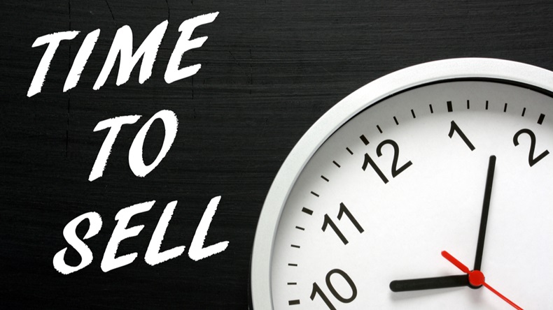 The words Time To Sell in white text on a blackboard next to a modern wall clock as a reminder - Image 