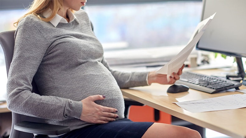 pregnancy, business and work concept - smiling pregnant businesswoman sitting at office table and reading papers